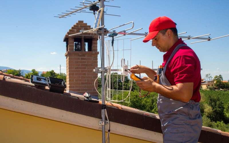 A technician on a house roof adjusting an antenna mast