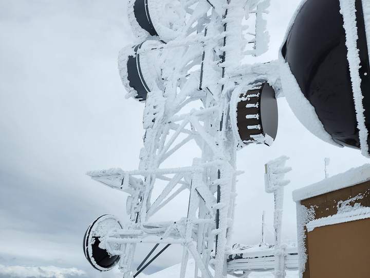 A rime-iced lattice tower with microwave dishes at a mountaintop radio site after a winter storm, March 2024
